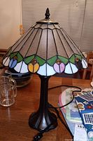 Front and side view of stained glass style lamp on a table showing detailed shade colors and metal base.