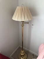 Full view of brass toned floor lamp with cream pleated fabric shade showing overall height and design.
