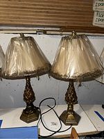 Two matching pineapple glass table lamps with beige fabric shades wrapped in plastic, placed side by side on a white surface.