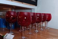 Photo of 10 ruby red crystal stemmed goblets showing full set in line on a shelf.