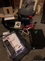 Wide view showing all items in the lot including Shop Vac, Garmin Nuvi 42 box, Jugreat safe, Samsung DVD player with remote, and a sealed digital camcorder box.