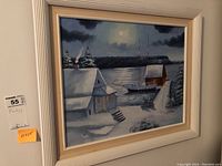 Framed oil painting depicting a snow-covered harbor at night with two sailboats and houses, measuring 21x25 inches.