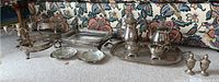 Wide shot showing weighted sterling silver salt and pepper shakers, coffee and tea pots, creamer, sugar bowl, silver tray, candelabras, and other serveware items on patterned fabric background.