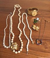 Multiple vintage pearl necklaces, decorative pins, pendant necklace, and Citizen quartz watch arranged on a brown surface.