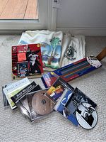 Lot contents including folded California Raisins and Billerica Indians shirts, Red Sox Talking StarCard baseball card in packaging, wooden cribbage board, and six music CDs arranged on carpet.