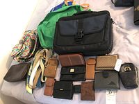 Overview of wallets, bags, belts laid on a bed including a black laptop bag and colorful tote bags
