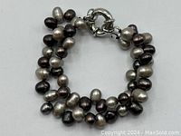 Double-strand bracelet made of brown and gray freshwater cultured pearls laid flat with circular clasp closure visible