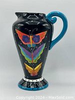 Front view of tall ceramic jug vase with butterfly design and blue handle.