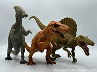 Front view of three vinyl dinosaur figures: Parasaurolophus left, Tyrannosaurus Rex center, Spinosaurus right. All posed standing.