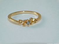 Close-up photo of gold tone floral ring centered with clear Swarovski crystal on a plain white background.