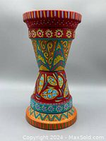 Front view of handpainted clay plant stand showing vibrant red, blue, yellow, and turquoise patterns with floral and geometric motifs.