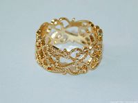 Close-up front angle photo of the gold tone filigree wide band ring, highlighting lace scroll detail and bead accents.