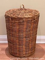 Full view of the large wicker cane hamper with lid and handle, showing its cylindrical shape and natural finish.