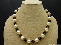 Front view of the vintage necklace on a beige display bust showing the pattern of large round faux pearls alternating with darker faceted topaz beads and gold dividers.