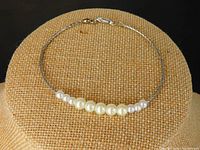 Full view of the pearl bracelet displayed on a woven beige stand, showing the pearl arrangement and silver clasp.