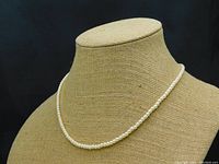 Necklace displayed on stand showing uniform small cream pearls, approximately 3 mm in diameter, 24 inches long.