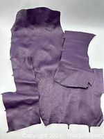 Three irregular pieces of purple leather laid flat to show size and shape.