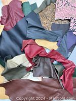 Various irregular-shaped small leather pieces laid out, showcasing different colors and textures including burgundy, green, grey, red, and patterned pieces.