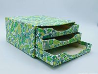 Front and side view of the mini chest with the bottom drawer pulled out showing the floral fabric covering and drawer handles.