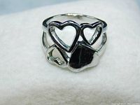 Close-up view of polished stainless steel ring showing one solid heart and three connected open hearts design, ring laid flat on white surface.