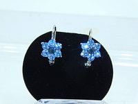 Front view of the vintage blue rhinestone earrings showing the floral petal design with lighter blue stones around a central darker blue stone on a silver tone setting, displayed on a black earring stand.
