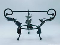 Black metal three-legged plant stand viewed from above and side, showing circular rings and decorative leaves and berries