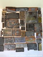 Top view of 40 vintage metal printing plates of various sizes and wooden block backings arranged in a square grid pattern
