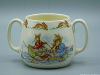 Full view of vintage two-handled bone china mug with running bunny pattern around upper rim and main scene of rabbit family rowing boat on water.