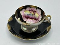 Teacup resting on saucer showing pink and gold floral pattern inside teacup, black and gold design on exterior and saucer.