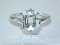 Front view of the ring showing the large emerald cut clear crystal with claw prongs and silver band.