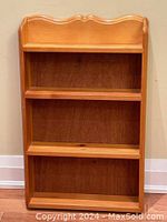 Full frontal view of the wood shelving unit showing 3 shelves, scalloped top edge and light brown finish.