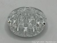 Clear round glass flower frog with multiple holes seen from an angled side view showing thickness and hole structure.