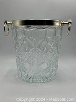 Front view of the heavy glass ice bucket showing the intricate cut-glass pattern and silver metal rim with handles.