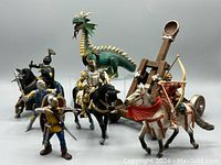 Group photo of all Schleich toys including knights on horses, standing knights, green dragon without wings, and wooden catapult.