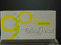 Top view of the Trivial Pursuit 1990's Edition box showing the design with yellow '90's lettering and grey dotted background.