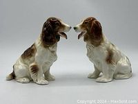 Front angle view of two ceramic Spaniel dogs sitting facing each other, showing brown and white coloring.