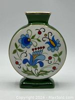 Round flat green porcelain vase with floral folklore design on the front, showing blue, red, yellow, and green flowers with gold trim around neck and base.