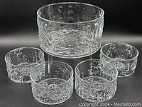 Five clear glass bowls on black background showing floral relief pattern; one larger bowl and four smaller bowls.