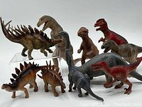 Ten assorted plastic dinosaur figures arranged on white background showing size and variety.