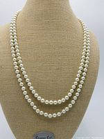 Knotted cream coloured imitation pearl necklace worn double strand on mannequin bust.
