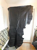 Full view of the large black leather hide held up for scale, showing its irregular shape.
