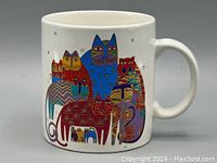 White ceramic mug decorated with colorful cats in various poses and patterns, gold accents visible on the design.