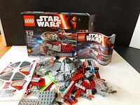 LEGO Star Wars 75135 set box, instruction manual, and loose pieces displayed, showing various LEGO bricks, some in sealed bags and stickers sheet.