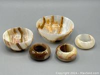 Two small onyx bowls and three onyx napkin rings arranged on a white surface, showing natural caramel and cream stone banding patterns.