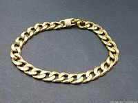 Full view of 10mm gold-colored Cuban link bracelet laid flat on dark surface showing overall condition and clasp detail.