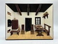Front view of handmade wood 3D diorama wall art showing kitchen living space with stove, chairs, table, bench, door, and window