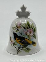 Front view of the white fine china bell showing detailed floral design and yellow-black bird with maple leaf handle.