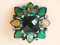 Front view of vintage Schreiner domed brooch showing layered green, aqua, smoke, and clear faceted glass stones with a dark central square stone.