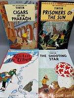 Four vintage TinTin comic books displayed flat showing front covers of Cigars of the Pharaoh, Prisoners of the Sun, TinTin in Tibet and The Shooting Star.