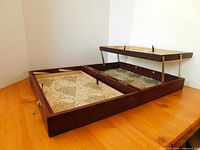 Wooden artist case opened flat with one hinged tray raised showing interior lining and tray supports.